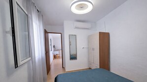 A bedroom with a bed, a wardrobe, an air conditioning unit, and a door leading to a bathroom.