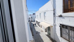 A narrow street with white buildings, a visible shop with a canopy, and a clear blue sky.