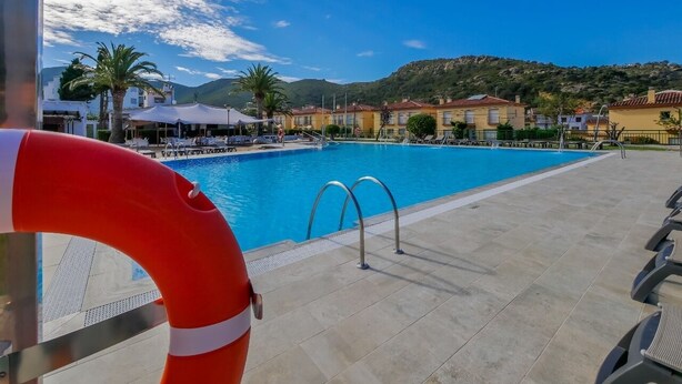 A swimming pool with clear blue water, surrounded by a tiled deck and a lifebuoy.