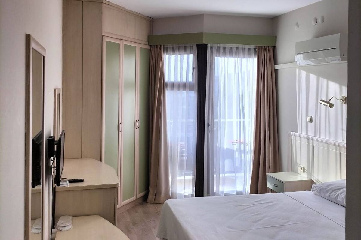 Una habitación de hotel con cama, escritorio, armario y ventana con cortinas.