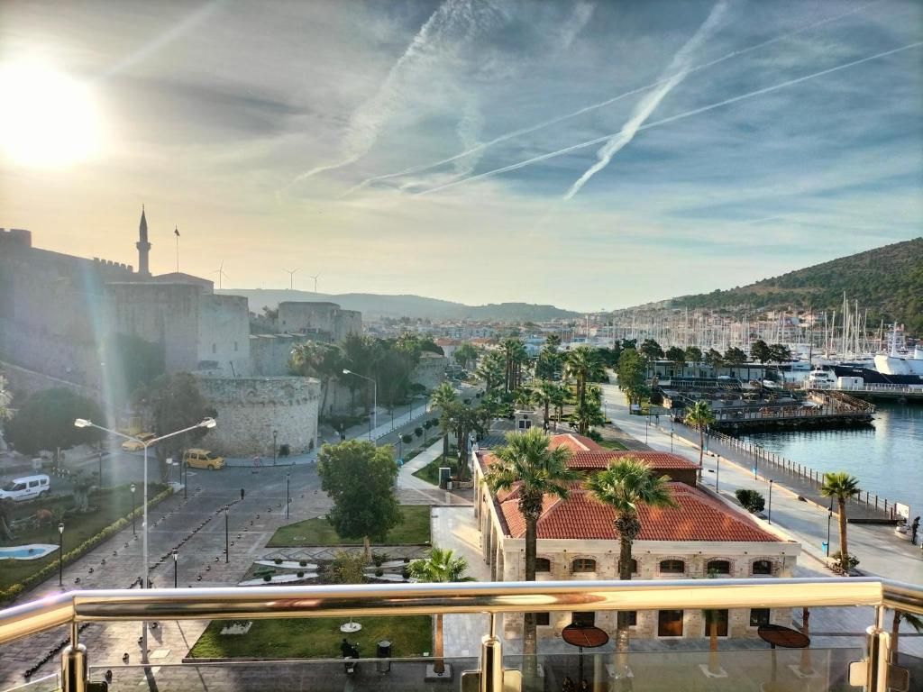 Un paysage urbain côtier avec un bâtiment historique imposant, une marina remplie de bateaux et un ciel dégagé.