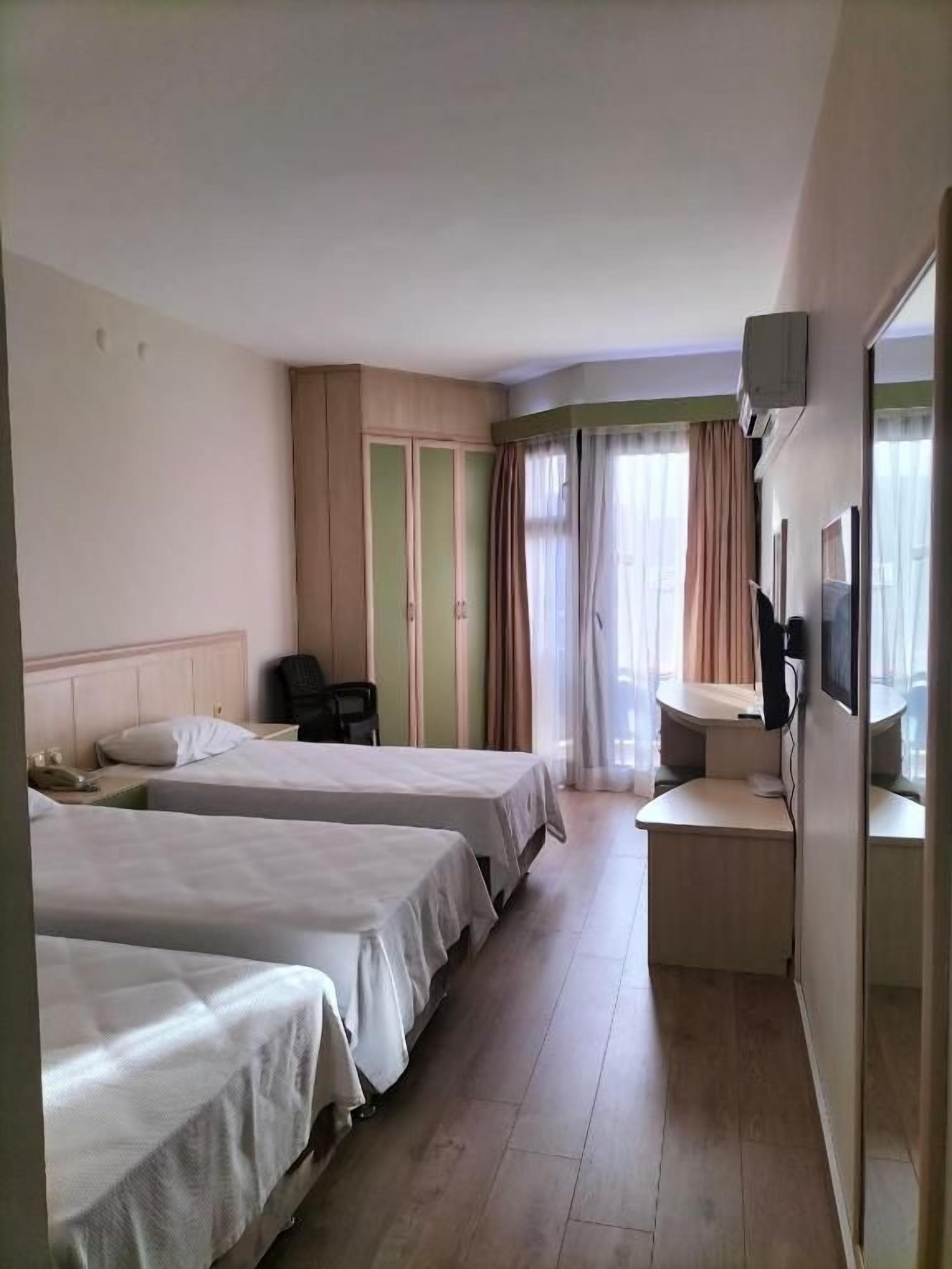 A hotel room with two beds, a desk, a chair, and a window with curtains.