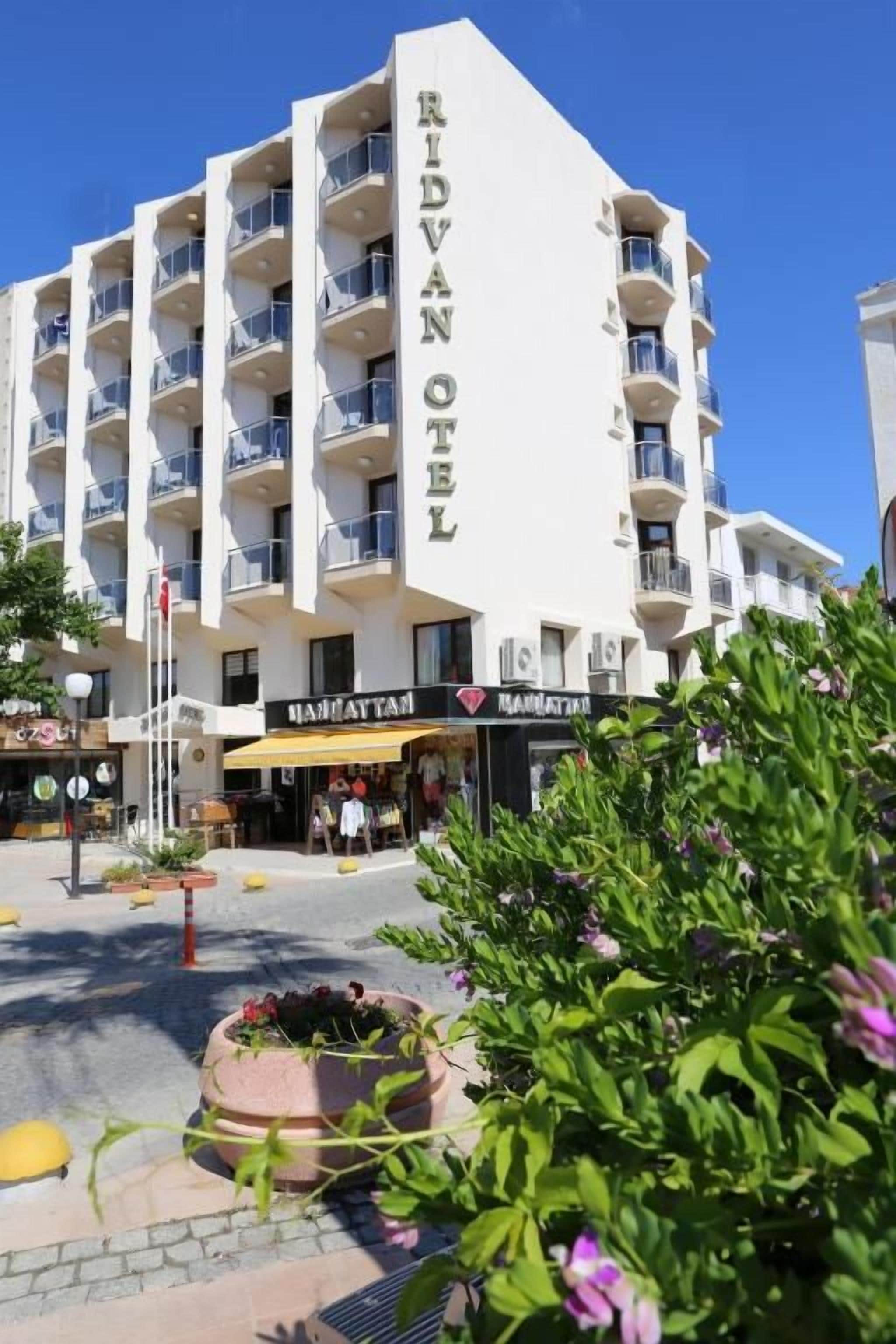 A multi-story hotel with balconies, a central entrance, and a flower bed in the foreground.