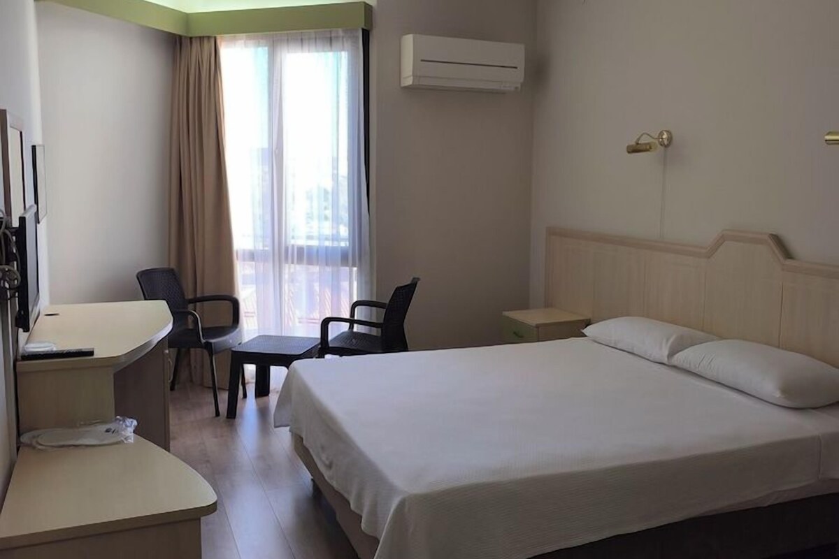 A hotel room with a bed, desk, chair, and an air conditioning unit.