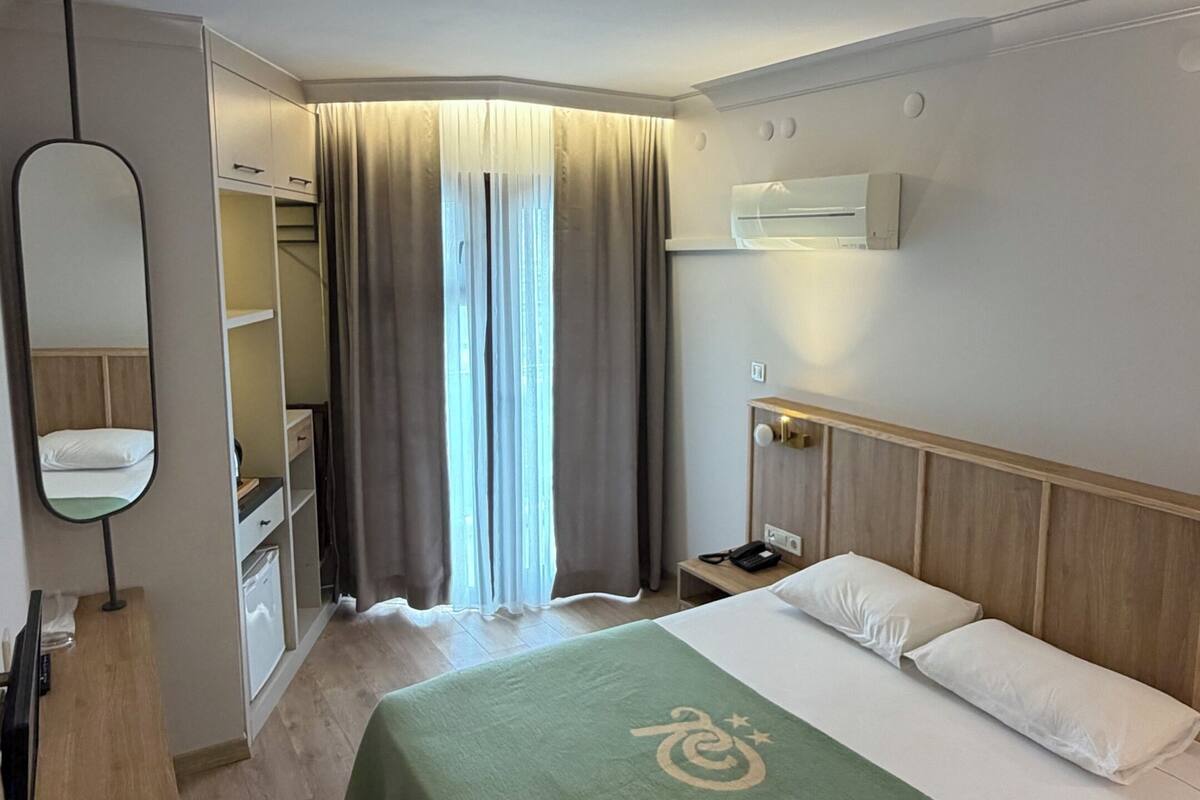 Una habitación de hotel con cama, escritorio, espejo, armario y ventana con cortinas.