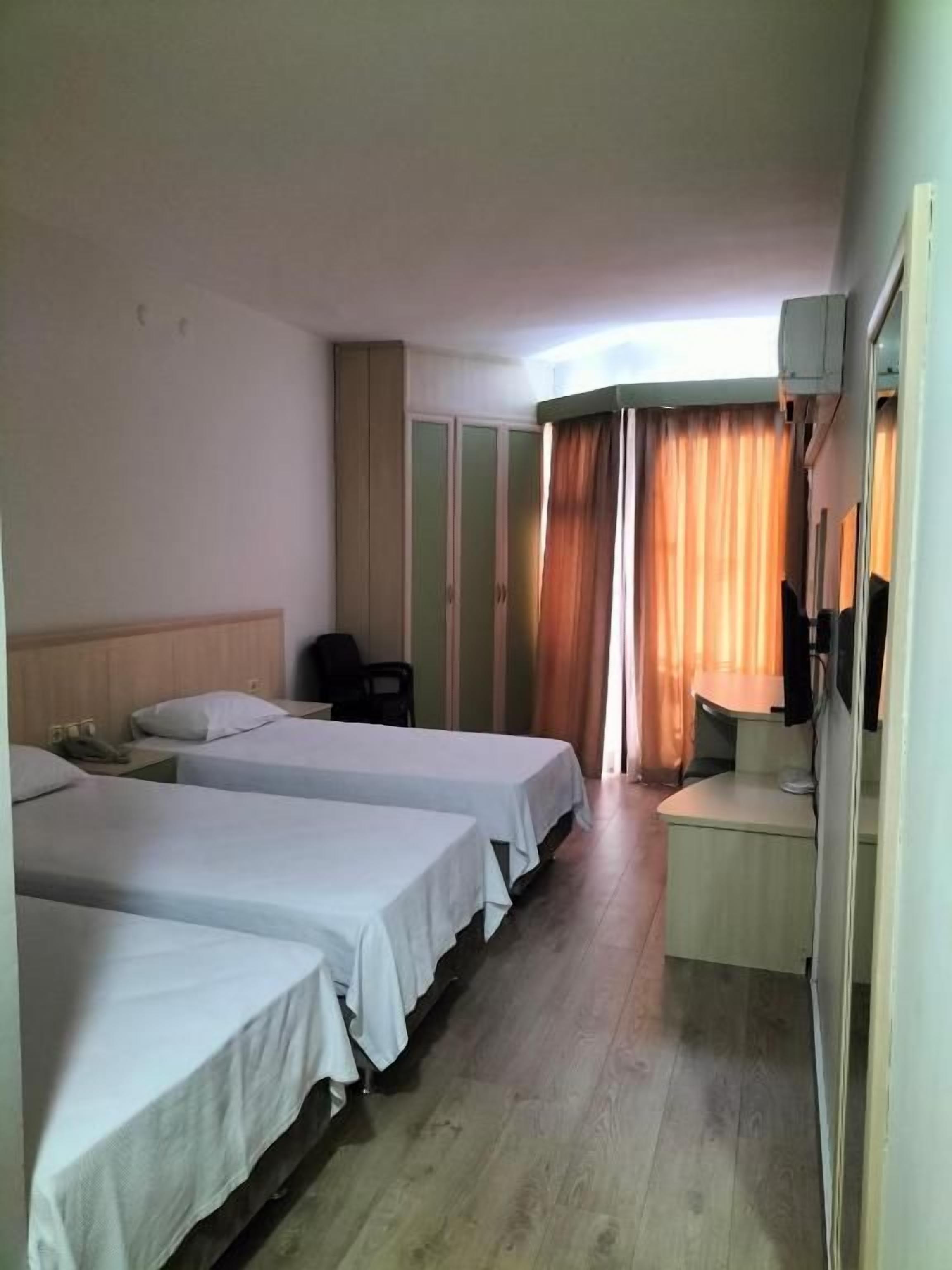 A hotel room with three single beds, a desk with a chair, a telephone, and a window with curtains.