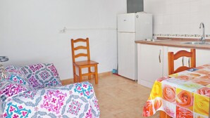 A small, compact room with a bed, a chair, a table, a kitchenette, and a window.