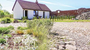 A single-story white house with a tiled roof, a stone wall in the background, and a gravel driveway. - Cozy home in Postomino with WiFi (Postomino)