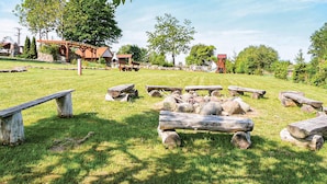 A rustic outdoor setting with a fire pit, wooden benches, and a stone structure in the background. - Cozy home in Postomino with WiFi (Postomino)