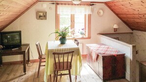 A cozy attic room with a wooden ceiling, a dining table with chairs, a television, and a window with lace curtains. - 3 bedroom lovely home in Lammhult (Lammhult)