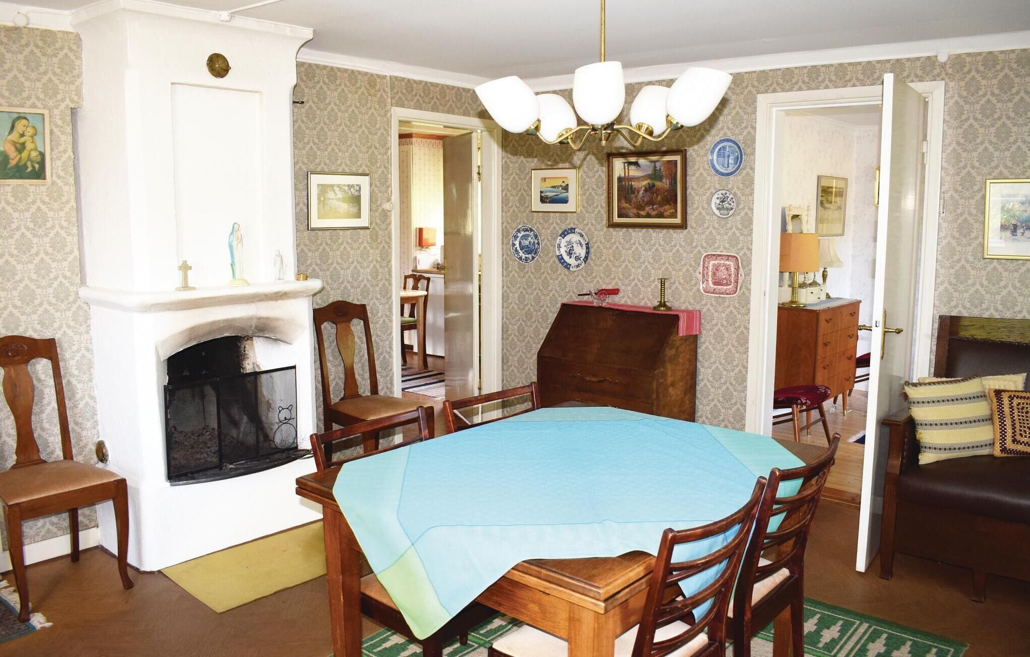 Une salle à manger avec une cheminée, des chaises en bois, une table recouverte d’une nappe bleue et un lustre.