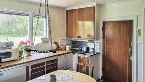 A compact kitchen with wooden cabinets, a microwave, a sink, and a dining area with a table and chairs. - 3 bedroom lovely home in Lammhult (Lammhult)