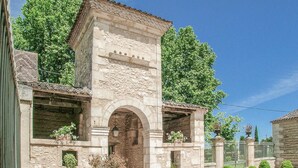 Un edificio de piedra con una entrada arqueada, techo de tejas y un área ajardinada con una reja.