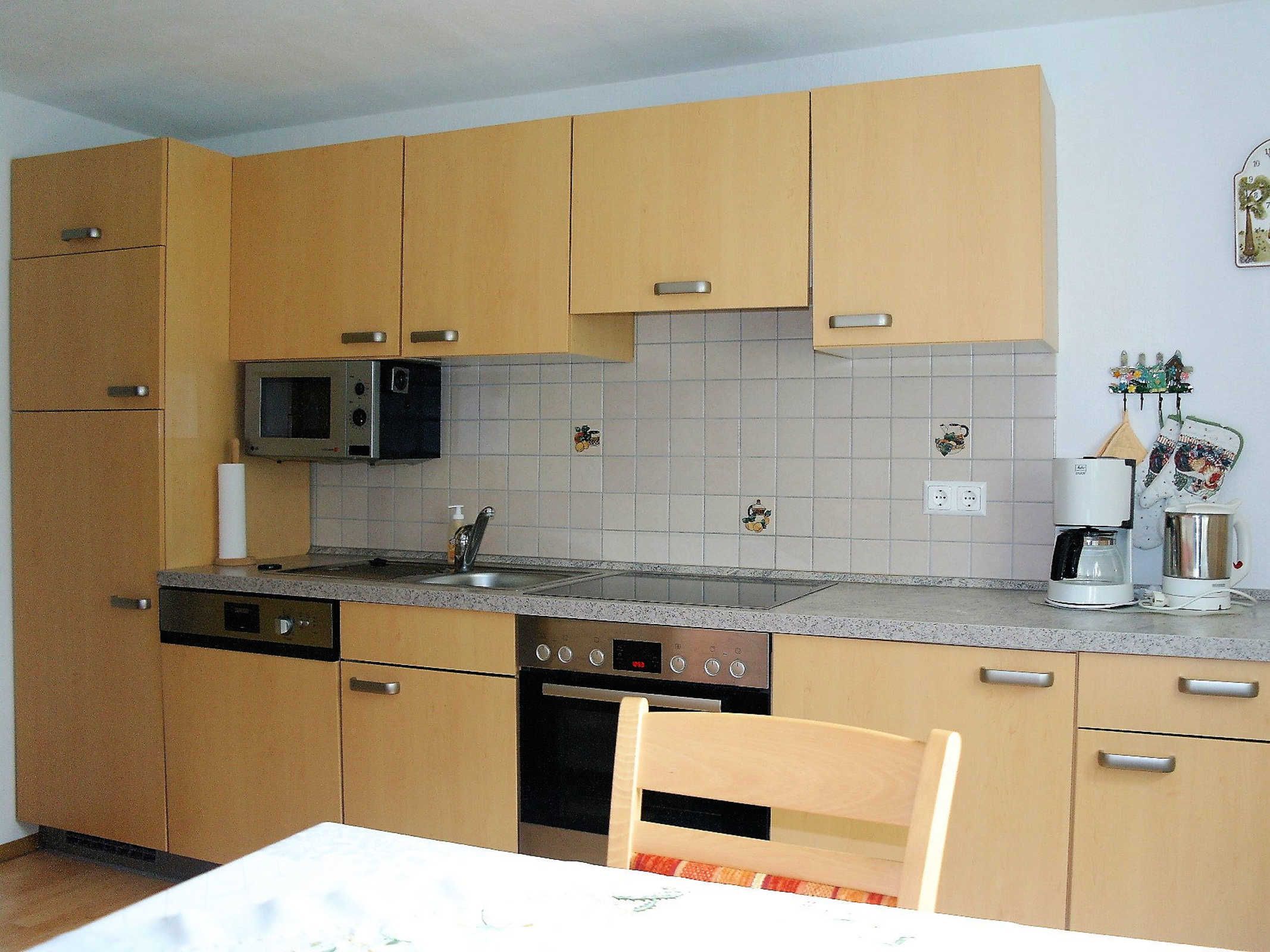 Una cocina compacta con armarios de madera, microondas, cafetera y lavavajillas.