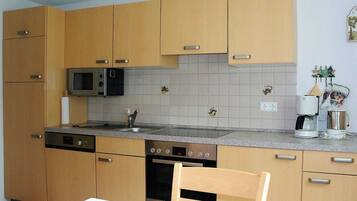 Una cocina compacta con armarios de madera, microondas, cafetera y lavavajillas.