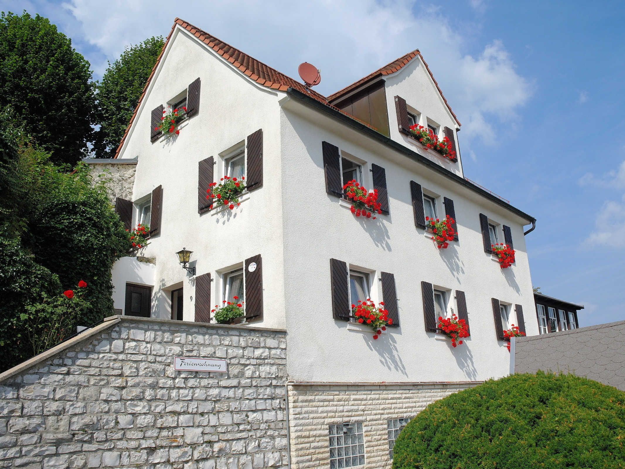 A multi-story building with stone walls, multiple windows with shutters, and flower boxes on the exterior.