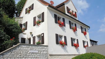 A multi-story building with stone walls, multiple windows with shutters, and flower boxes on the exterior.