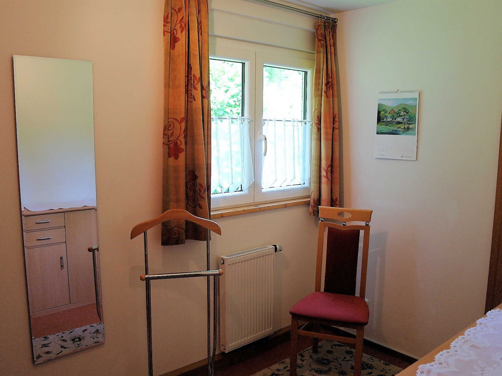 A room with a radiator, a wooden chair with a red cushion, a whiteboard on the wall, and a window with curtains.