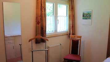A room with a radiator, a wooden chair with a red cushion, a whiteboard on the wall, and a window with curtains.