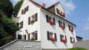Ein mehrstöckiges Gebäude mit Steinmauern, zahlreichen Fenstern mit Fensterläden und Blumenkästen an der Fassade.