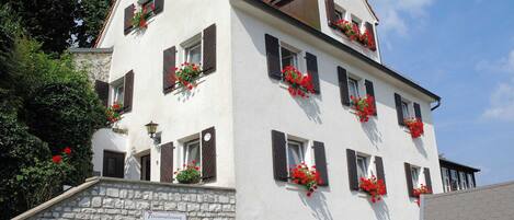 A multi-story building with stone walls, multiple windows with shutters, and flower boxes on the exterior.