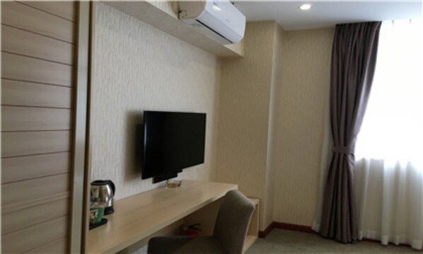 Une chambre d’hôtel équipée d’un téléviseur à écran plat fixé au mur, d’un bureau en bois, d’une chaise, d’une machine à café et d’une fenêtre avec des rideaux.