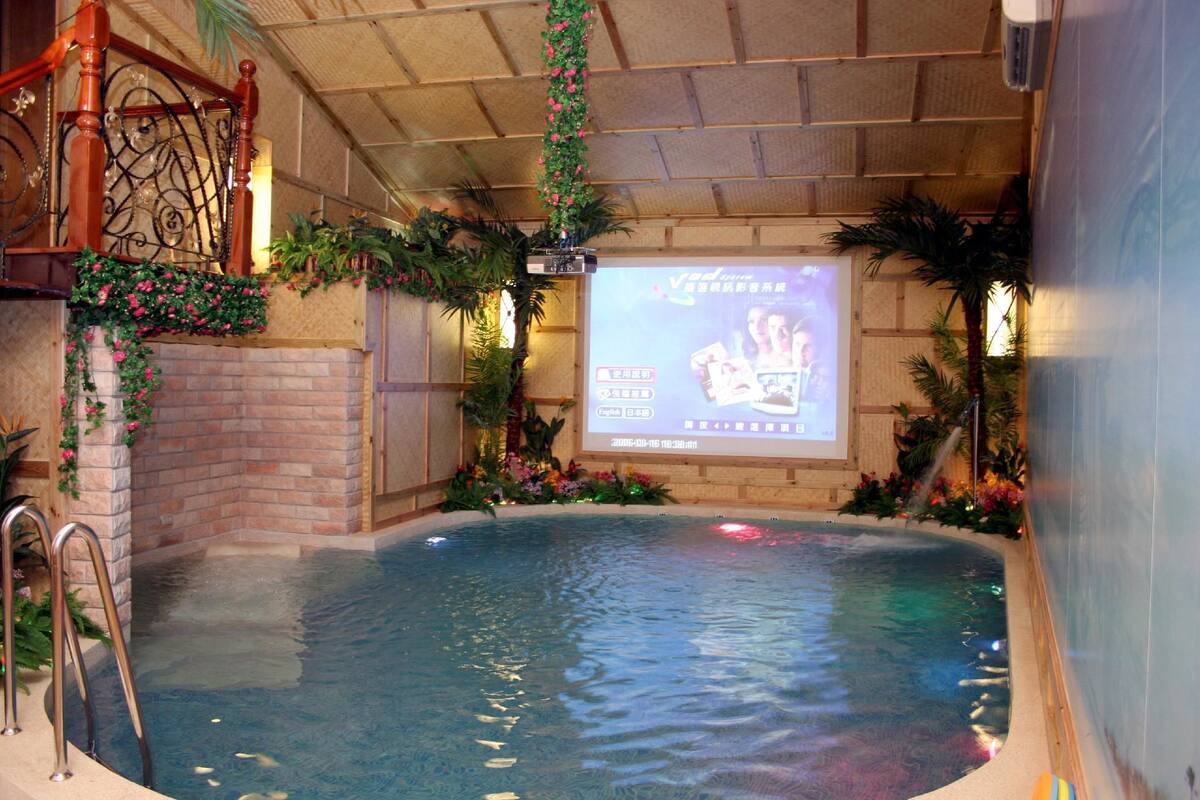 Une piscine intérieure avec un mur en briques, un escalier en bois et un écran de projection affichant du texte.
