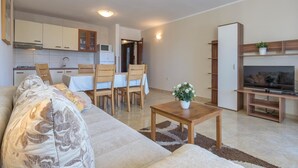 Un espacio habitable compacto con sofá, mesa de comedor, sillas, televisor y zona de cocina.