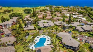An aerial view of a resort with multiple bungalow-style buildings, a central swimming pool, and a golf course visible in the background.