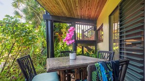 An outdoor patio with a table and chairs, surrounded by lush greenery and a wooden pergola.