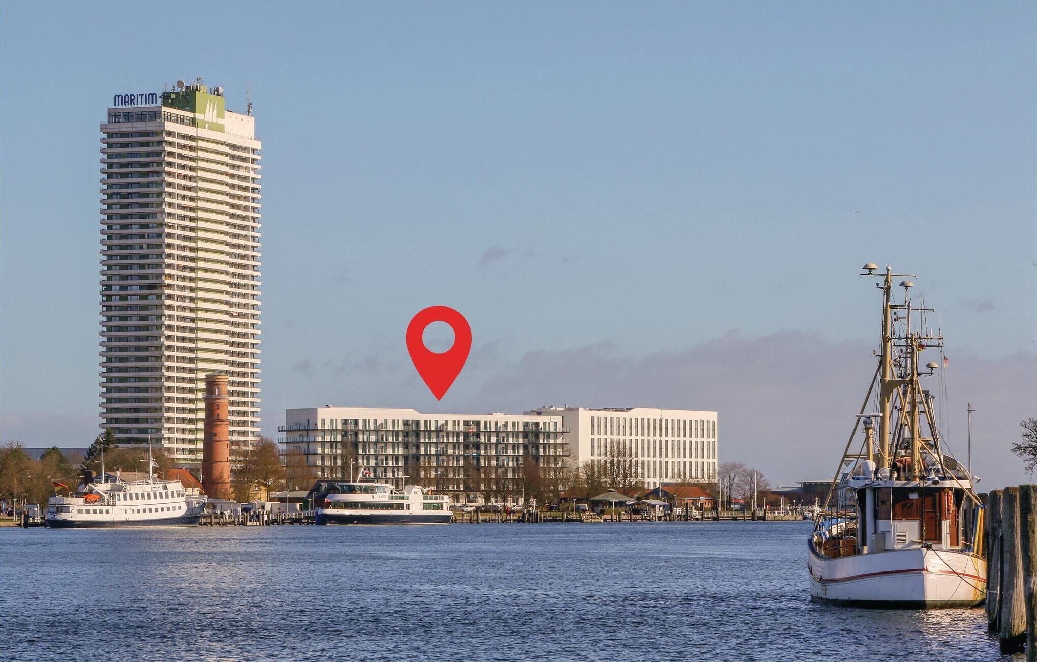 A tall building with a 'MARITIM' sign, a white building with a red location pin, and a boat docked at a pier.