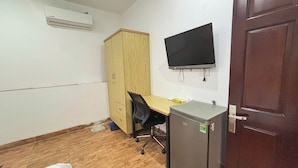 A small office space with a wooden wardrobe, a desk with a chair, a black monitor, and a refrigerator. - 95 Lam Son Hotel (Ho Chi Minh City)