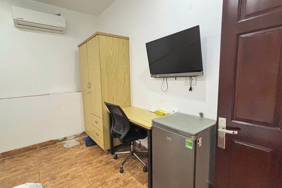 Un petit bureau comprenant une armoire en bois, un bureau avec une chaise, un écran noir et un réfrigérateur.