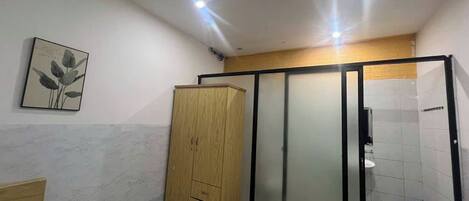 A small, compact bathroom with a wooden cabinet, a sliding glass door shower, and a tiled floor.