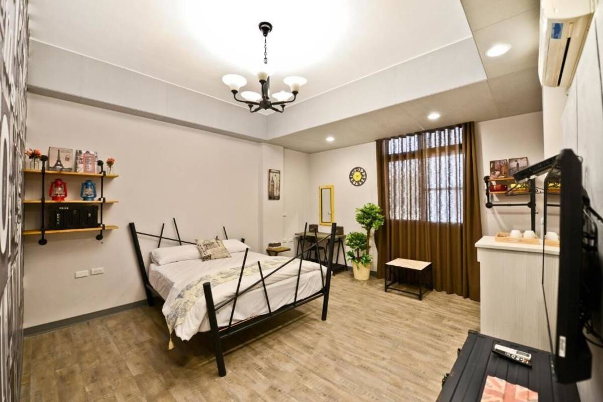 A bedroom with a bed, a desk, a chair, a potted plant, a shelf with books, and a clock on the wall.