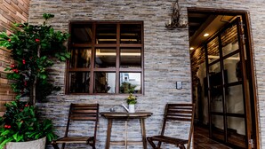 A brick wall with a window, two wooden chairs, a small table, and a potted plant with red berries. - England Garden (Tainan)
