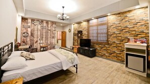 A bedroom with a bed, a TV, a small cabinet, and a stone wall. - England Garden (Tainan)