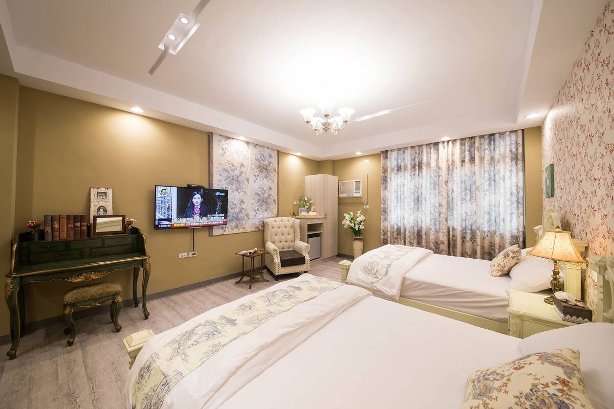 A hotel room with two beds, a desk with a chair, a television, and a wardrobe.