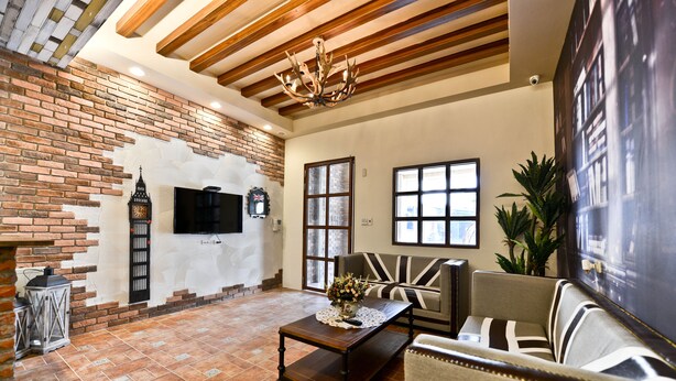 A spacious living room with exposed brick walls, a large flat-screen TV, a wooden ceiling, and a comfortable seating area with a sofa and armchairs. - England Garden (Tainan)