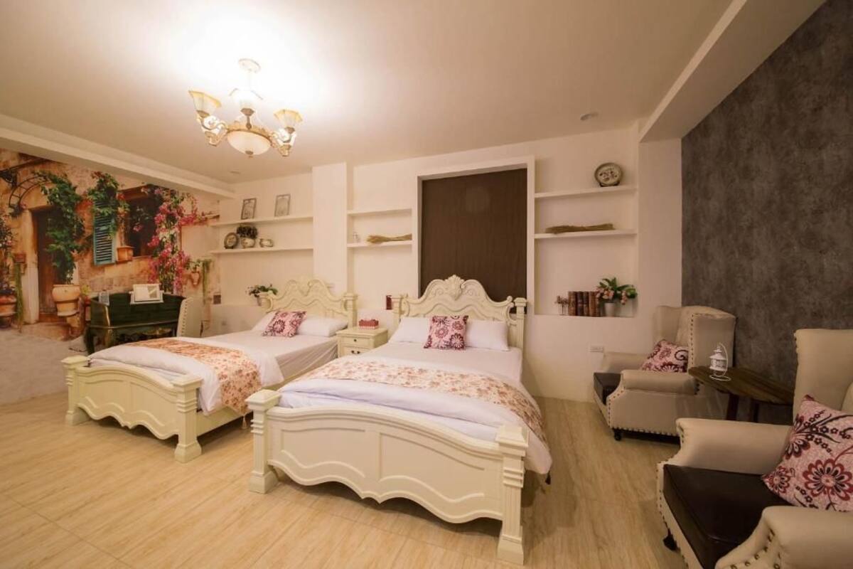 A bedroom with two white beds, a chandelier, a chair, and shelves with decorative items.
