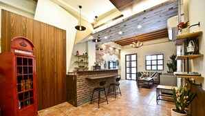 A spacious room with a wooden ceiling, a brick wall, and a red telephone booth. There is a bar area with stools and a potted plant. - England Garden (Tainan)
