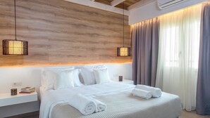 A modern hotel room with a large bed, white linens, a wooden headboard, two hanging lamps, a nightstand, and a window with curtains.