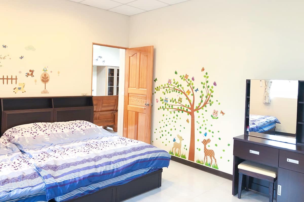 A bedroom with a bed, a dresser, a mirror, and a wall with a tree mural.