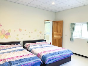 Un dormitorio con dos camas, una puerta de madera, una ventana con cortinas y una pared decorada con motivos florales.