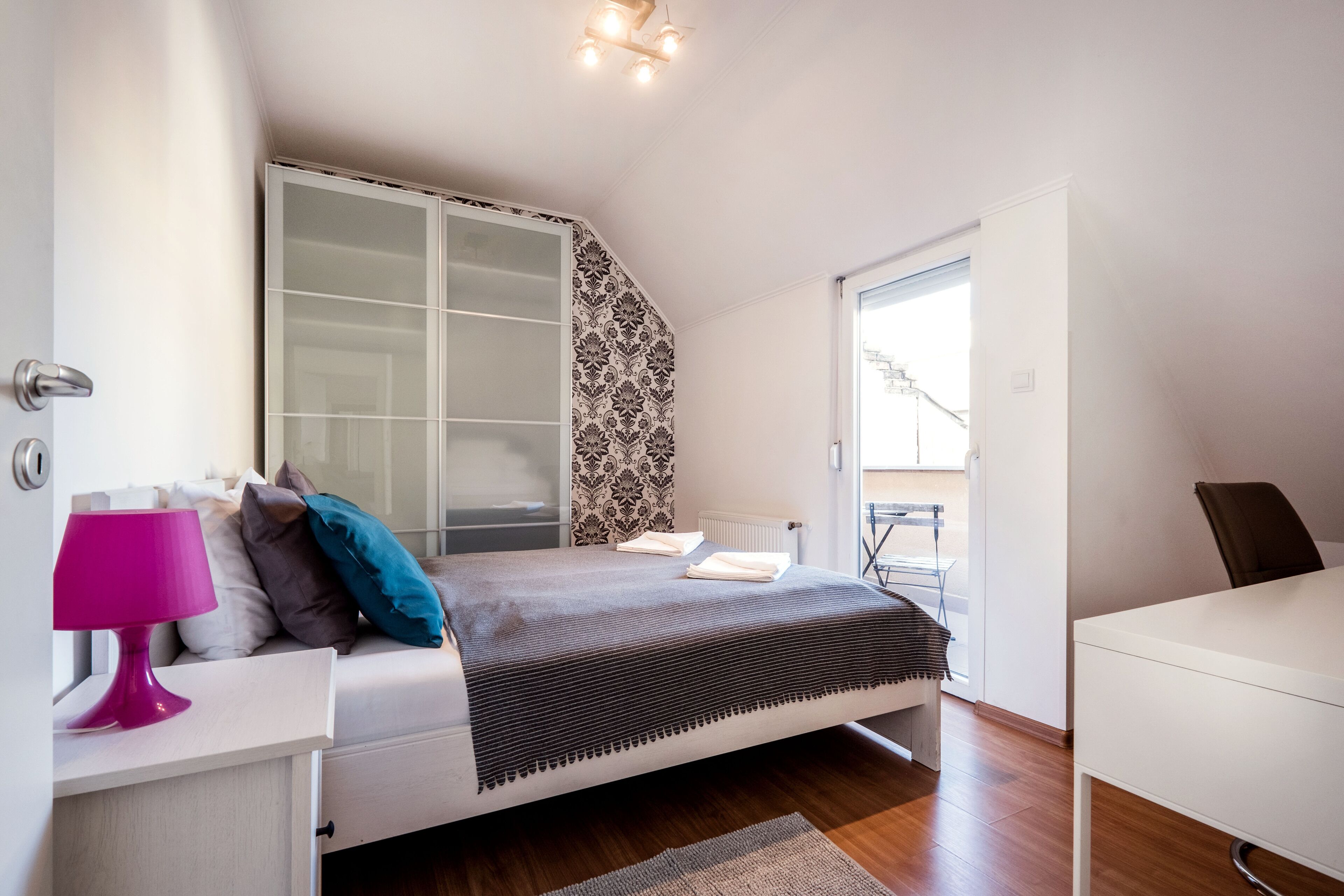 Quarto com cama, mesa de cabeceira, abajur, guarda-roupa e uma cadeira.