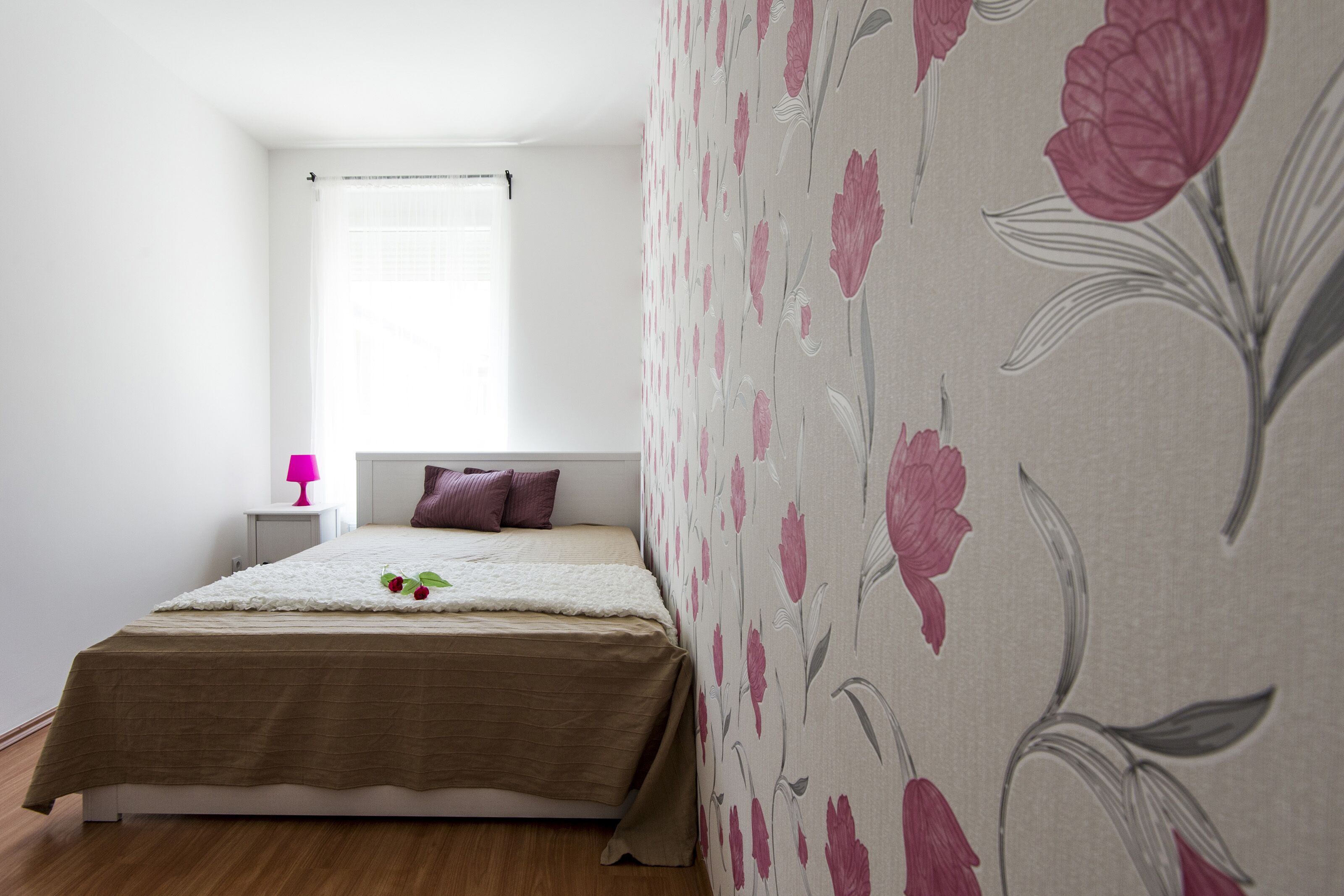 A bedroom with a bed, a nightstand, a lamp, and a window with a curtain.