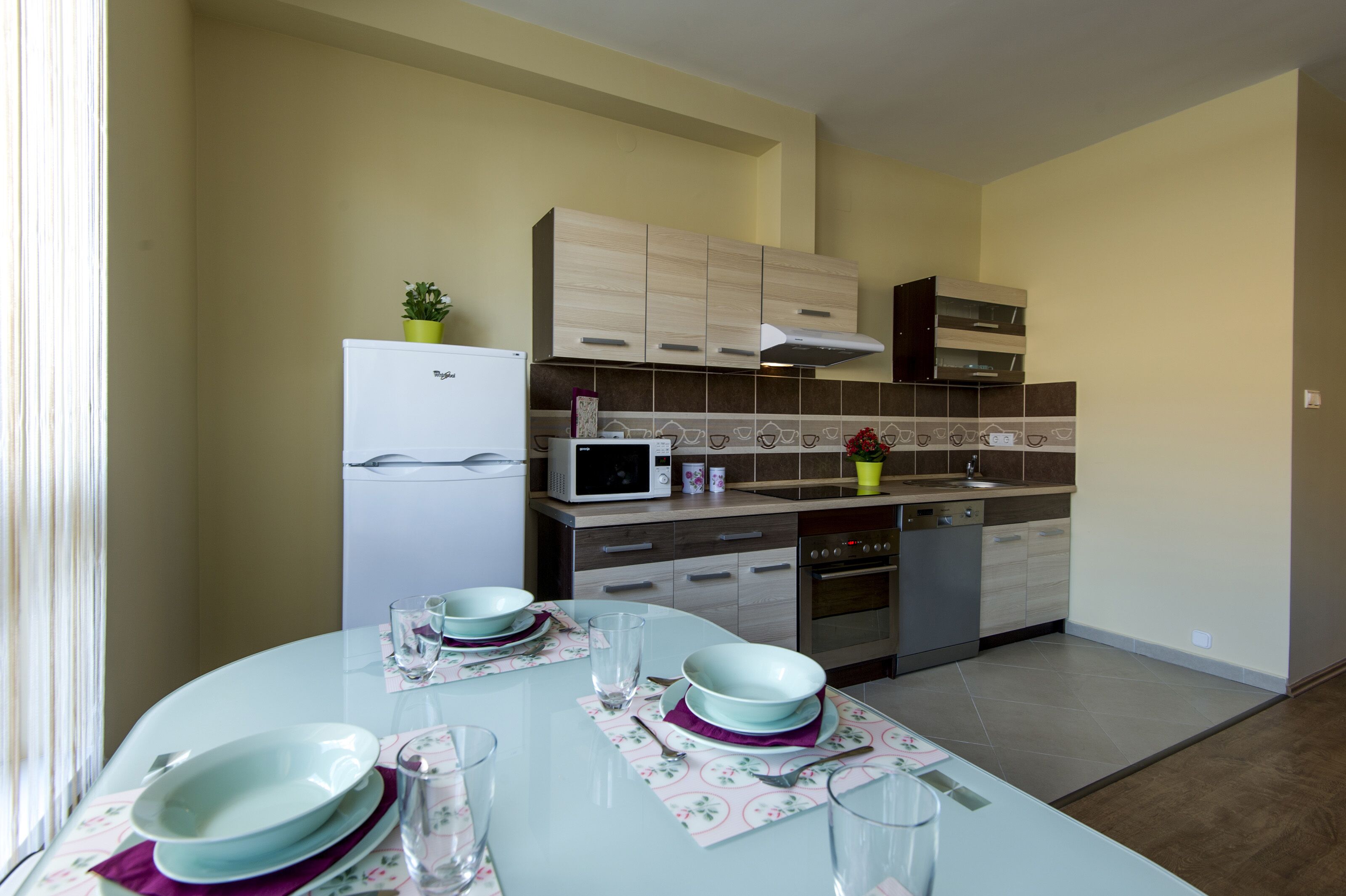 Una cocina moderna con un refrigerador blanco, microondas y horno. Hay una mesa de comedor con platos, vasos y cubiertos.