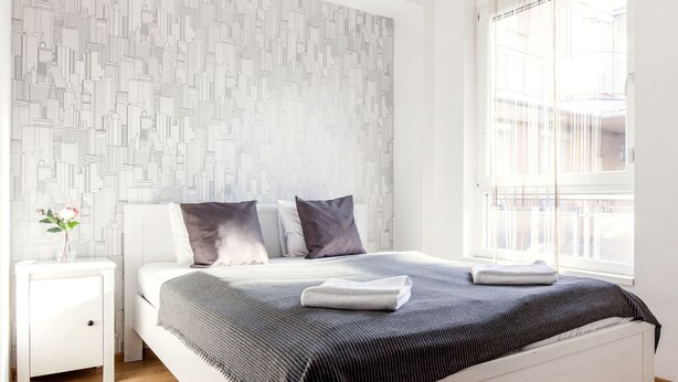 Un dormitorio moderno con una cama grande, una mesita de noche, una ventana con cortinas y una pared con estampado.
