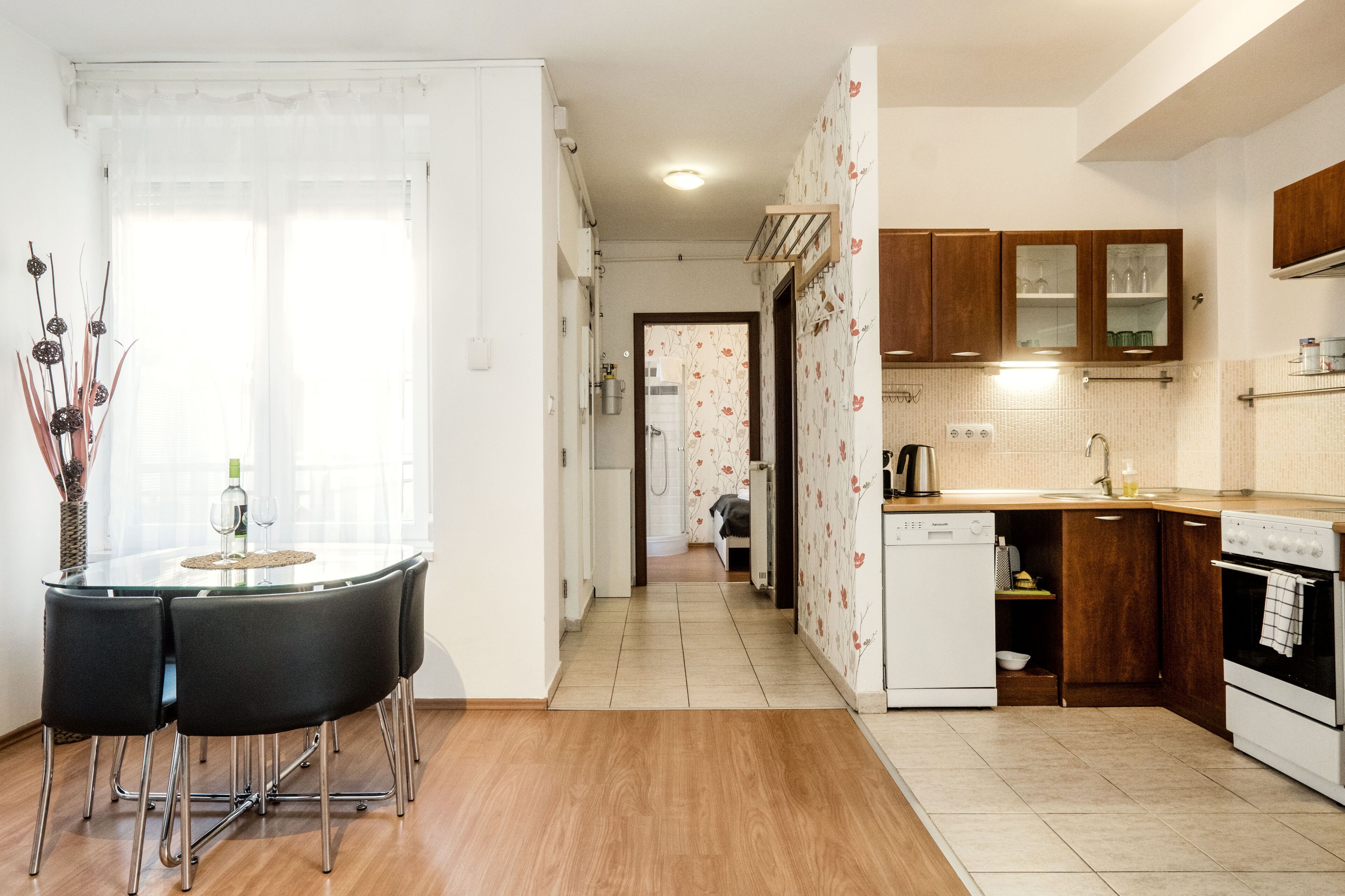 A modern kitchen with wooden cabinets, a dishwasher, and a dining area with a glass table and chairs.