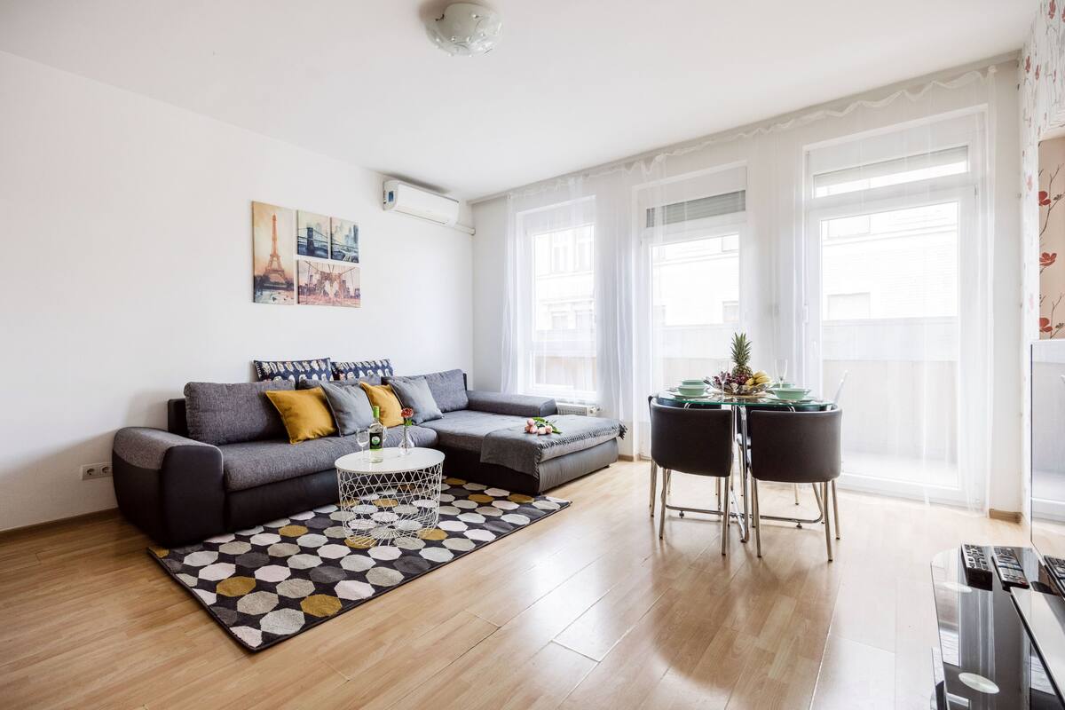 A modern living room with a grey sofa, a coffee table, and a dining area with two chairs.